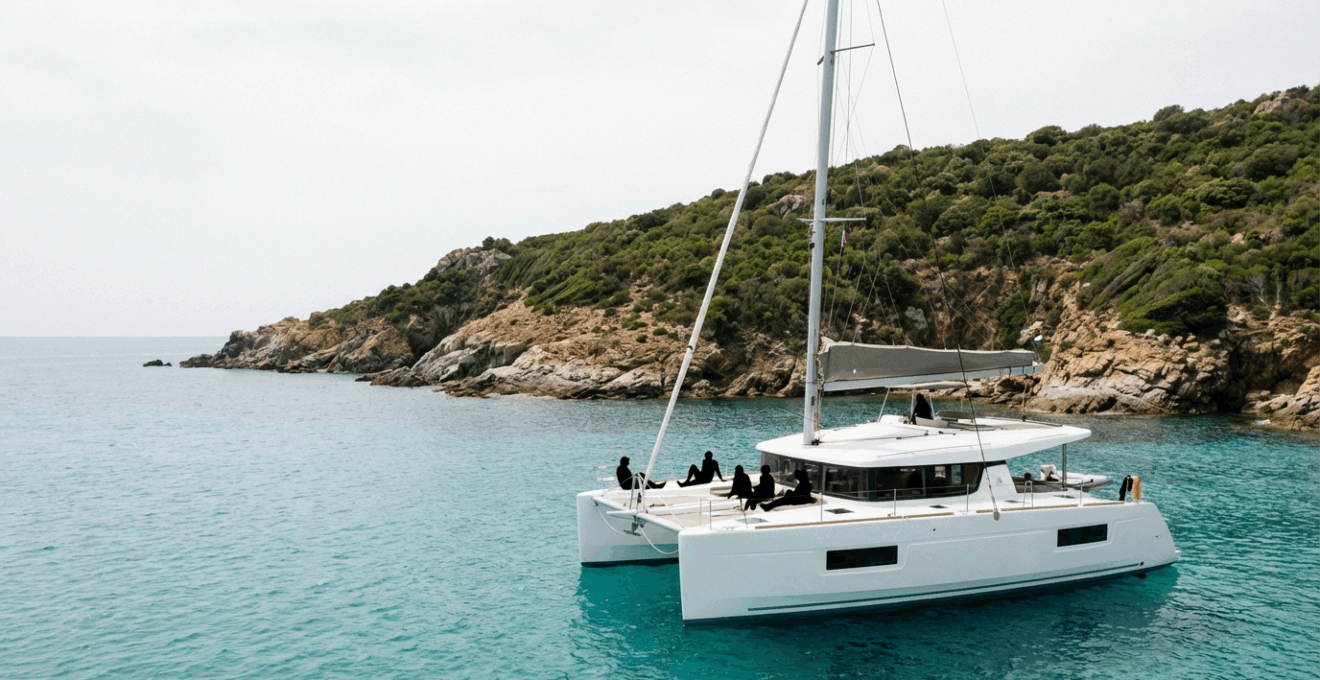 Catamaran naviguant le long des côtes rocheuses de Corse avec passagers sur le pont