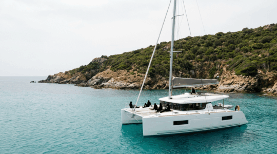 Catamaran naviguant le long des côtes rocheuses de Corse avec passagers sur le pont
